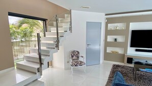Una sala de estar moderna con una escalera que lleva a un balcón, un televisor y una silla decorativa.
