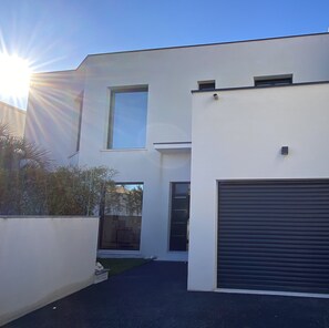 A modern two-story building with a garage, large windows, and a clear sky.