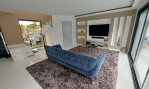 A modern living room with a sofa, a flat-screen TV, and a staircase leading to another level.