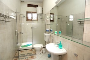 Een badkamer met een douchecabine van glas, een toilet, een wastafel en een glazen plank met toiletartikelen.