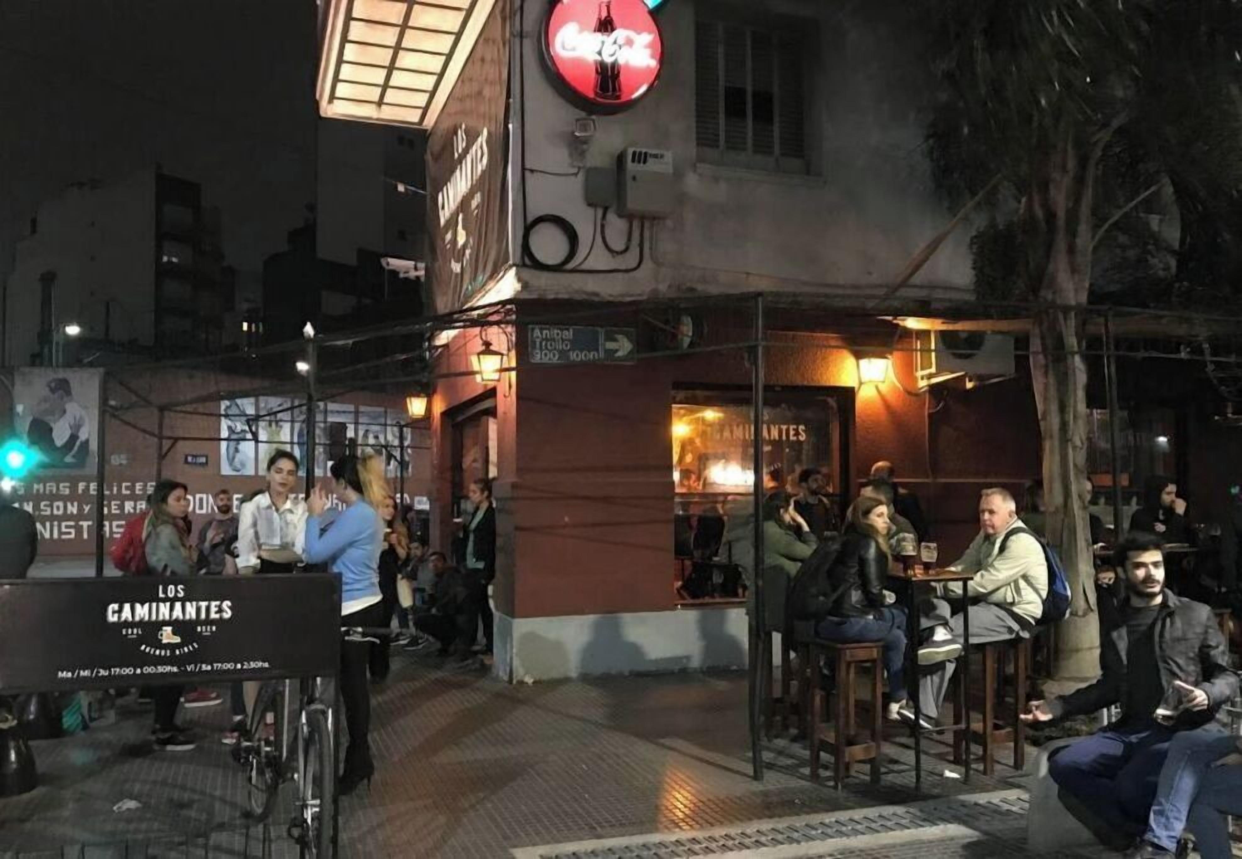 Área externa com mesas e cadeiras em restaurante, um letreiro da Coca-Cola acima e um anúncio com a inscrição 'Los Gaminantes' abaixo.
