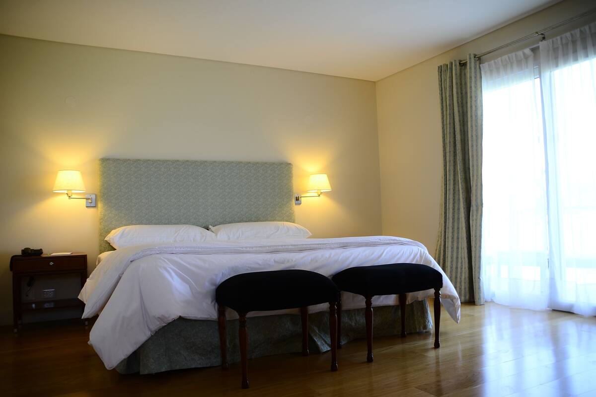 A neatly made bed with white linens, two bedside lamps, and a wooden nightstand with a lamp.