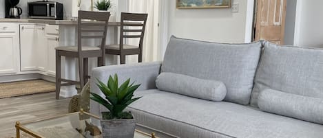 A modern living room with a grey sofa, a glass coffee table, and a dining area with chairs.