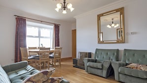 A living room with a dining area, wooden furniture, a large mirror, and a chandelier. - Matthews Traditional Holiday Cottage (Doonbeg)
