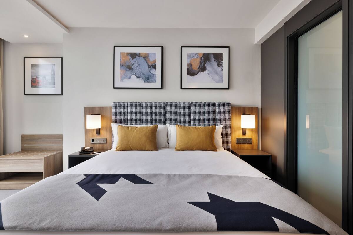 A modern hotel room with a large bed, two bedside tables with lamps, and abstract artwork on the walls.