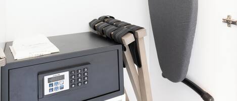 A hairdryer on a stand, a grey ironing board, and a black bag labeled "HAIRDRYER" on a white shelf.