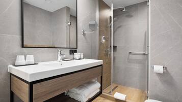 A modern bathroom with a large mirror, a white sink, and a glass-enclosed shower.