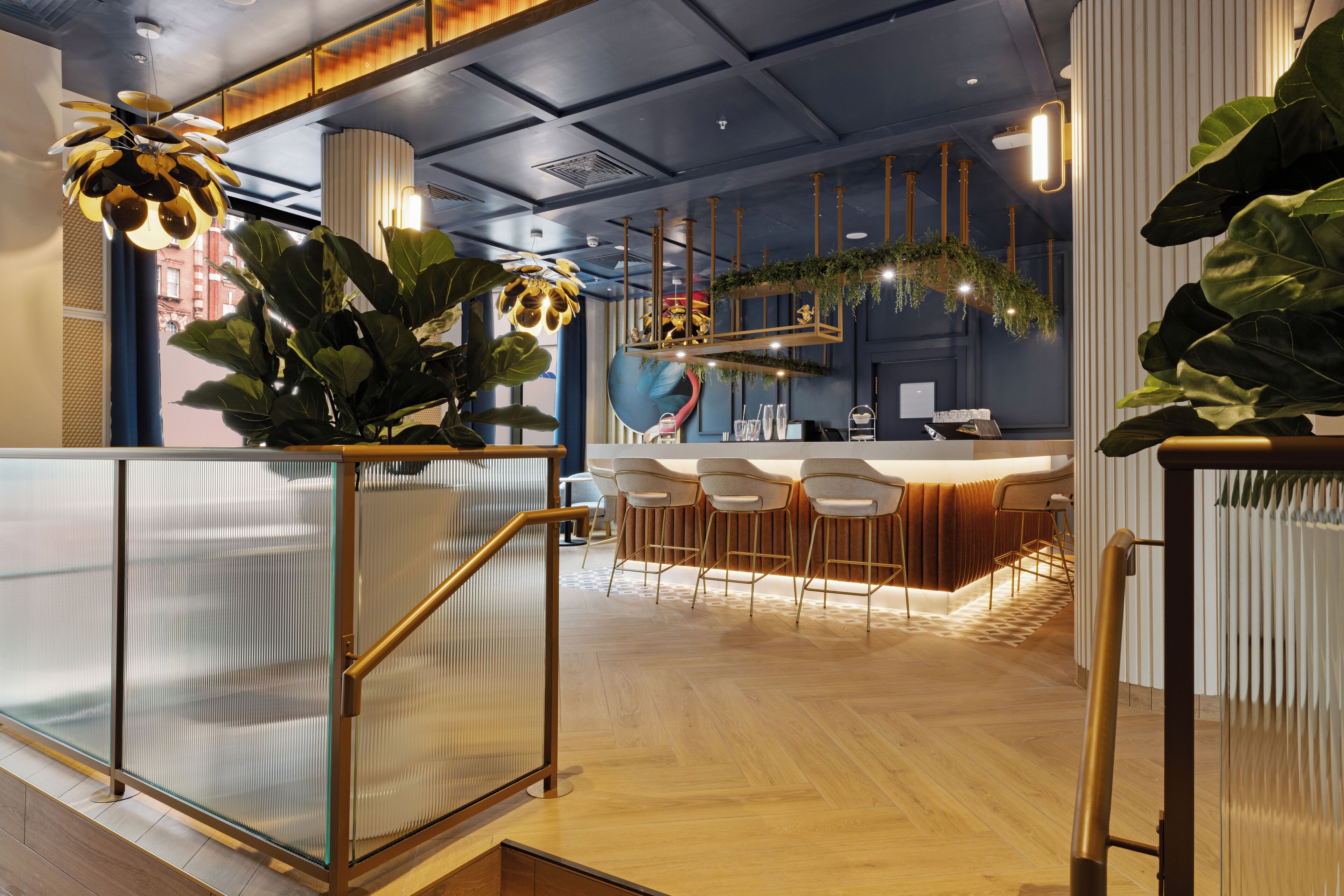 Uma área de bar moderna com piso de madeira, banquetas brancas e uma divisória de vidro.