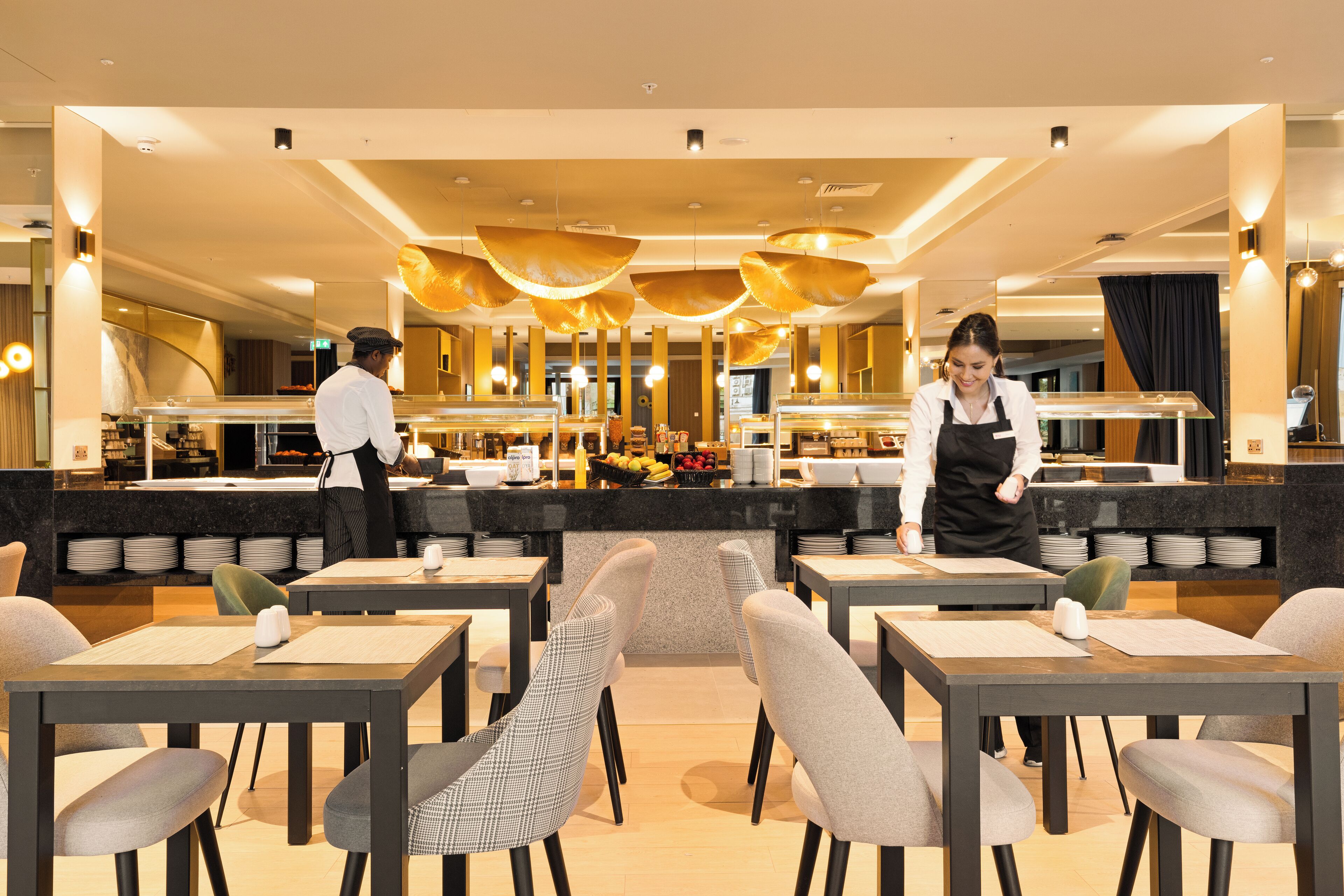 A modern restaurant with a central counter, multiple seating areas, and a bar.