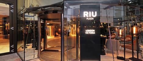 A glass entrance with a sign reading "RIU PLAZA LONDON VICTORIA HOTEL".