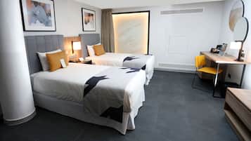 Habitación de hotel con dos camas, un escritorio, una silla, un espejo y obras de arte en las paredes.