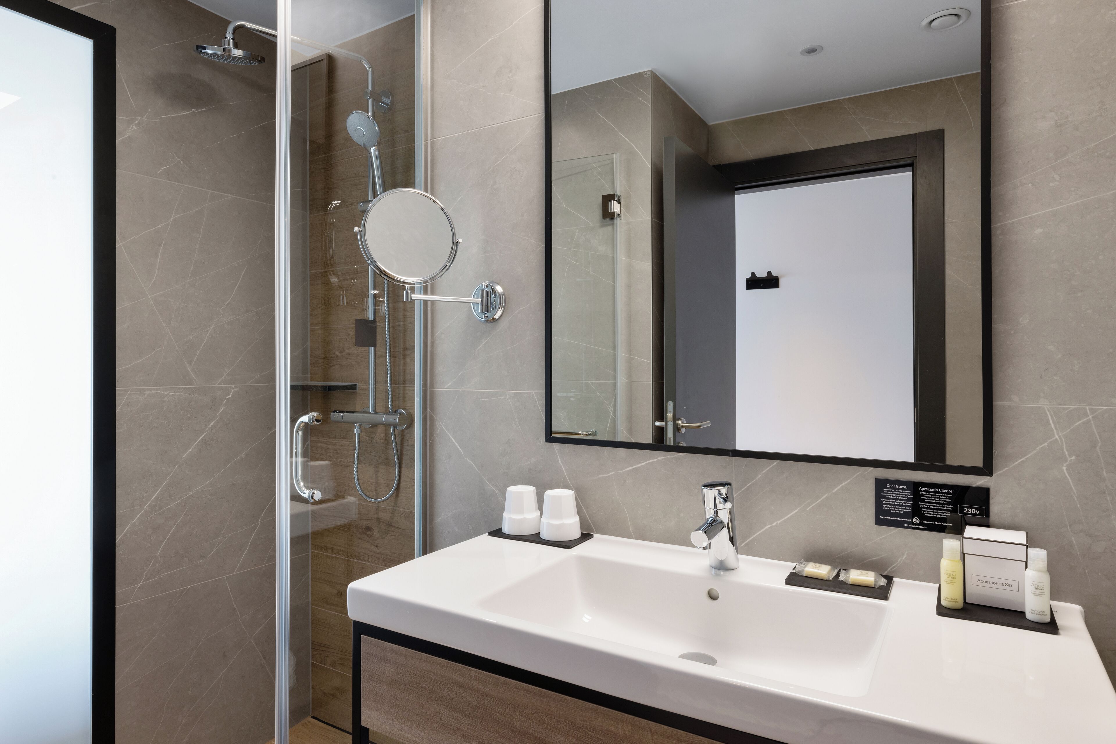 A modern bathroom with a large mirror, a shower with a handheld showerhead, and a sink with toiletries.
