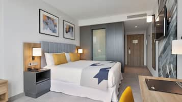 A modern hotel room with a large bed, bedside tables, a desk, and artwork on the walls.