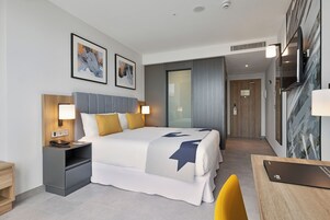 Una habitación de hotel moderna con una cama grande, mesitas de noche, un escritorio y obras de arte en las paredes.
