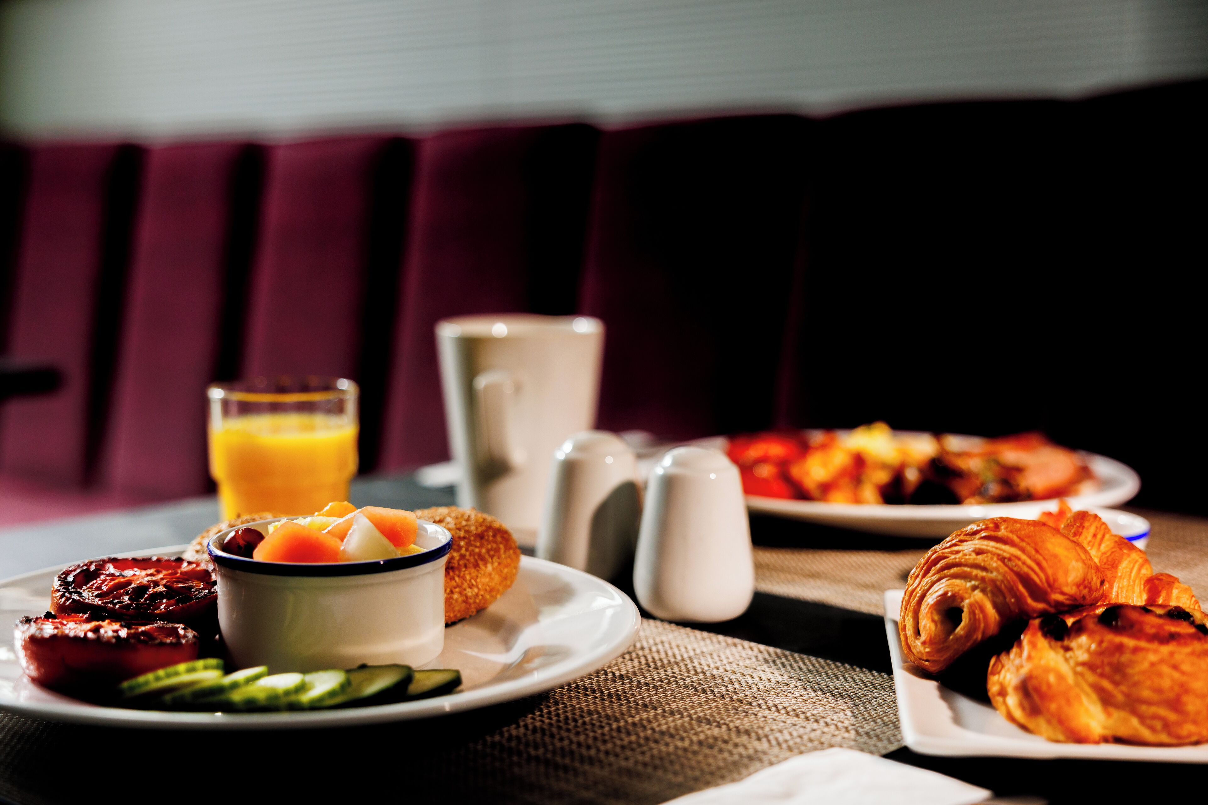 Une table dressée pour le petit-déjeuner, avec des assiettes remplies de nourriture, un bol de fruits, un verre de jus d’orange, ainsi que des salières et des poivrières.