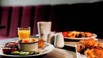 Una escena de desayuno con platos de comida, un bol de fruta, un vaso de zumo de naranja y saleros y pimenteros sobre una mesa.