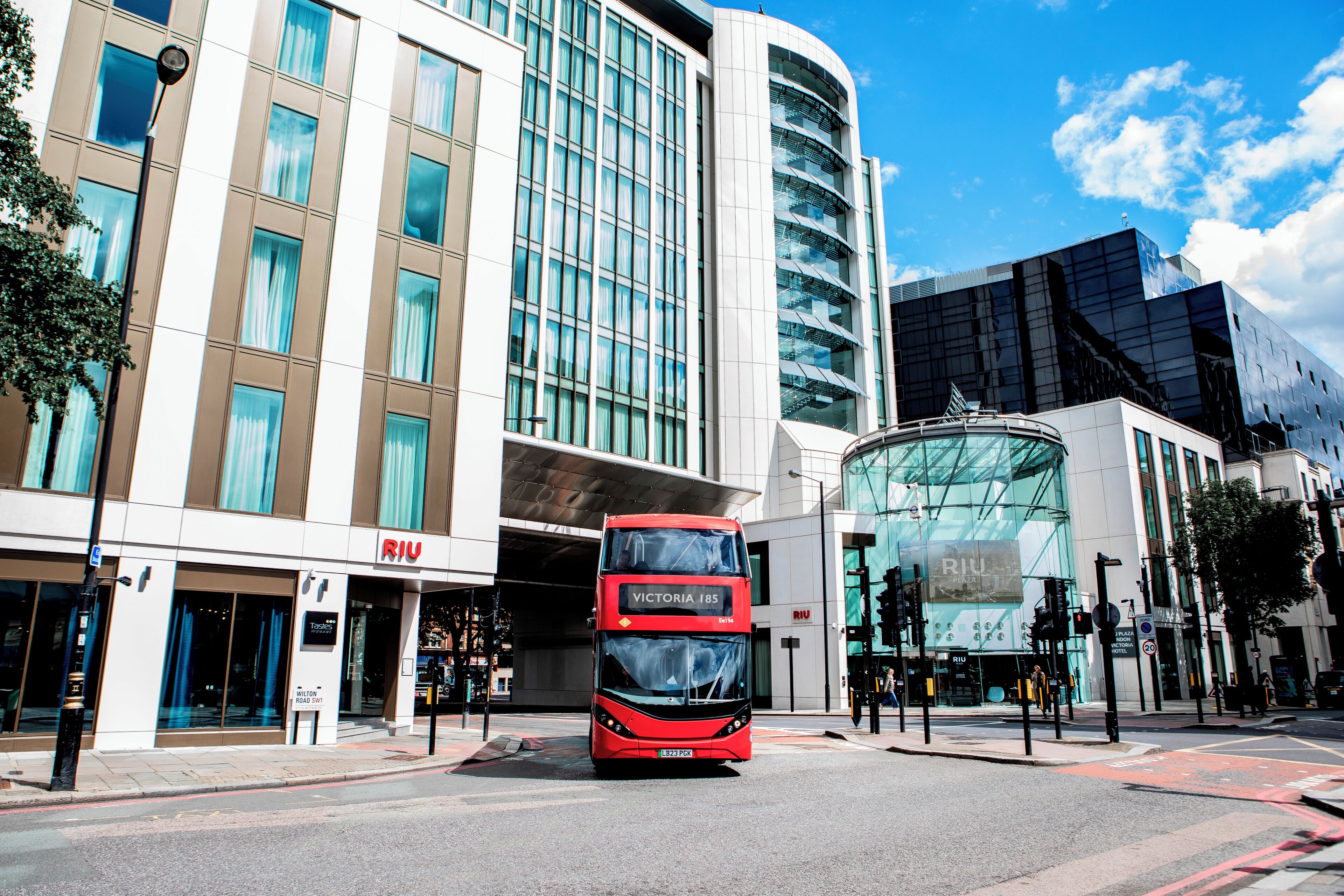 Un autobus à deux étages rouge se trouve devant un bâtiment moderne doté de grandes fenêtres et d’une façade en verre incurvée.