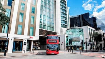 Un autobus à deux étages rouge se trouve devant un bâtiment moderne doté de grandes fenêtres et d’une façade en verre incurvée.