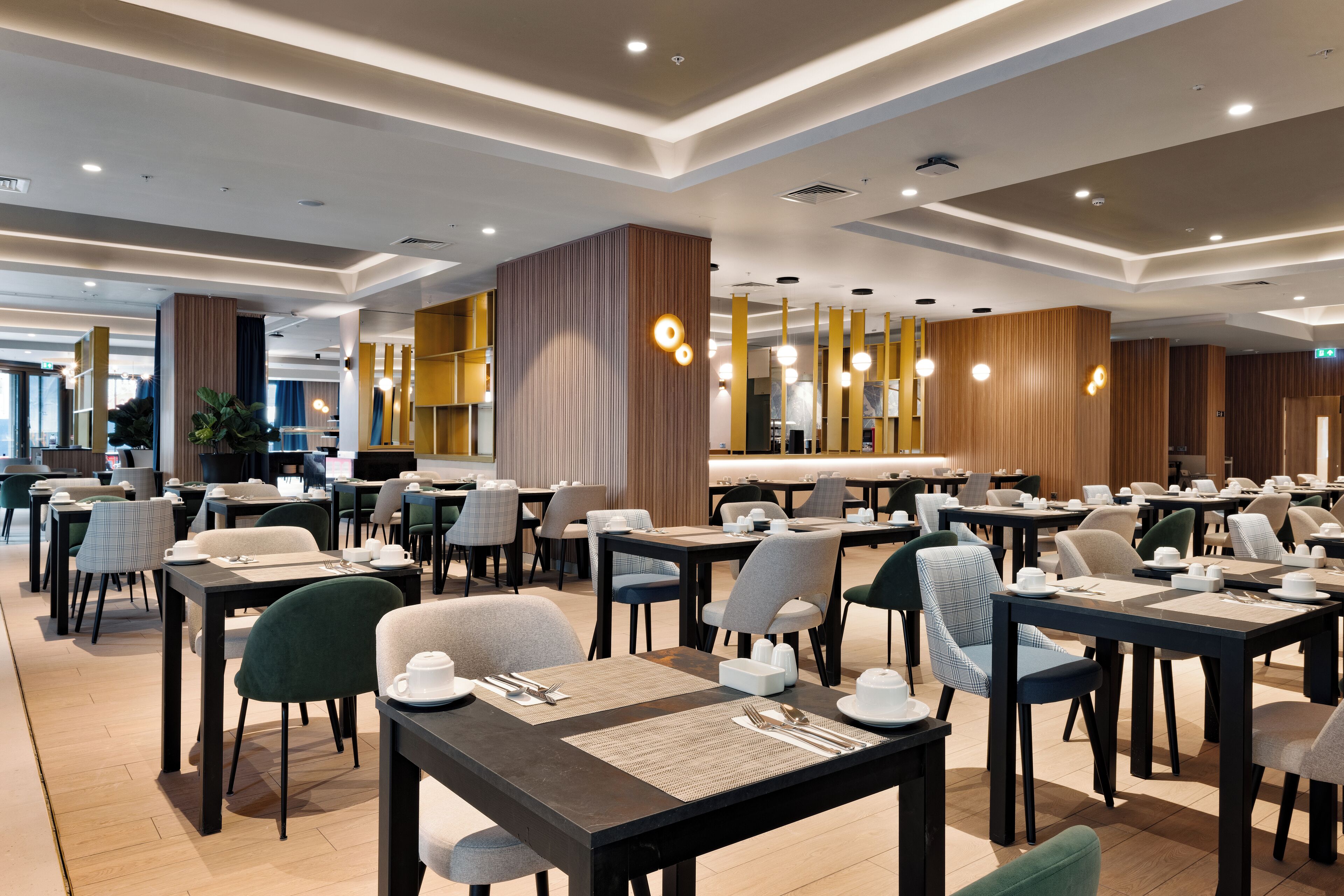 A modern dining area with multiple tables and chairs, wooden accents, and pendant lighting.