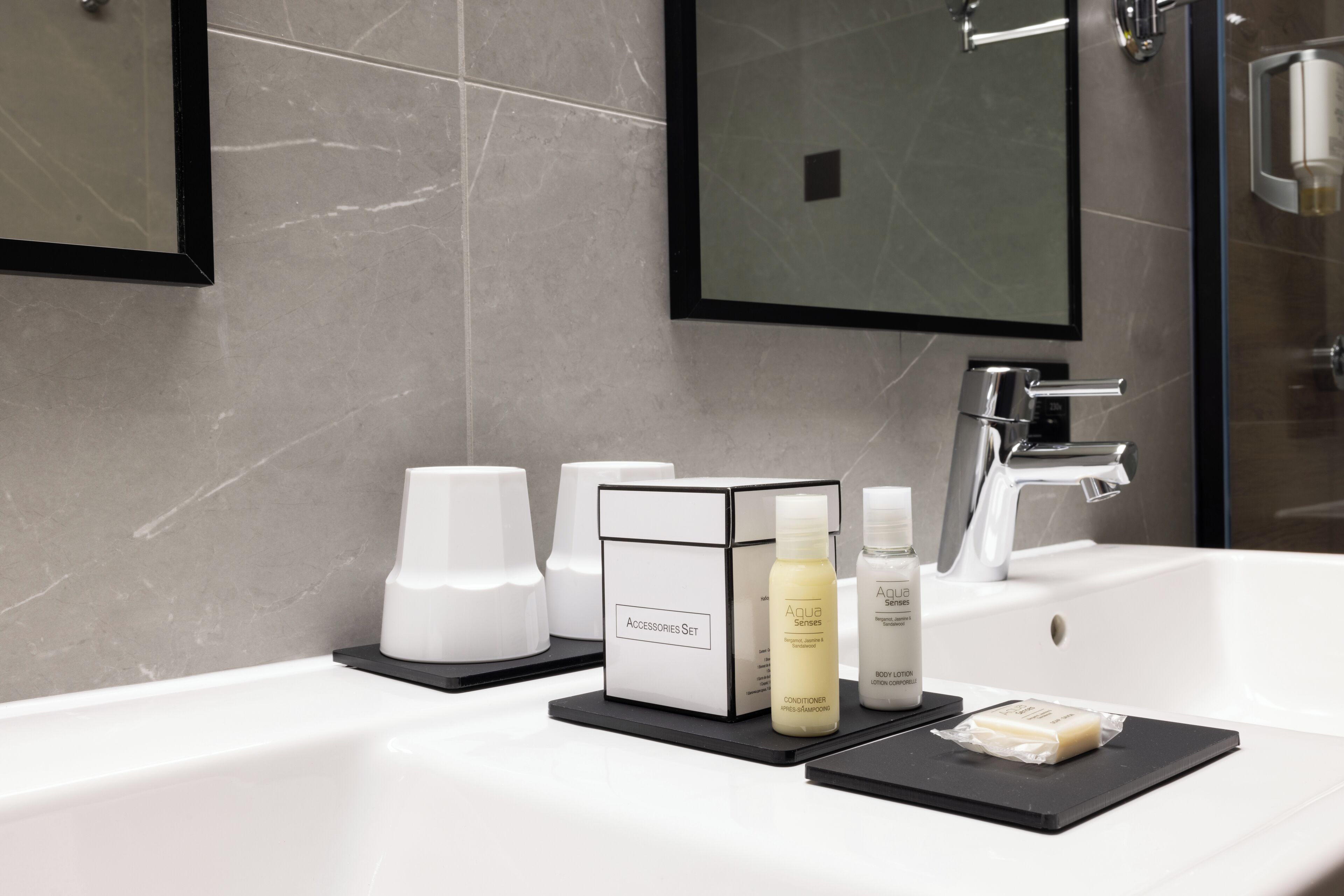 Un bagno moderno con uno specchio grande, un lavandino bianco e un vassoio nero con articoli da toilette.