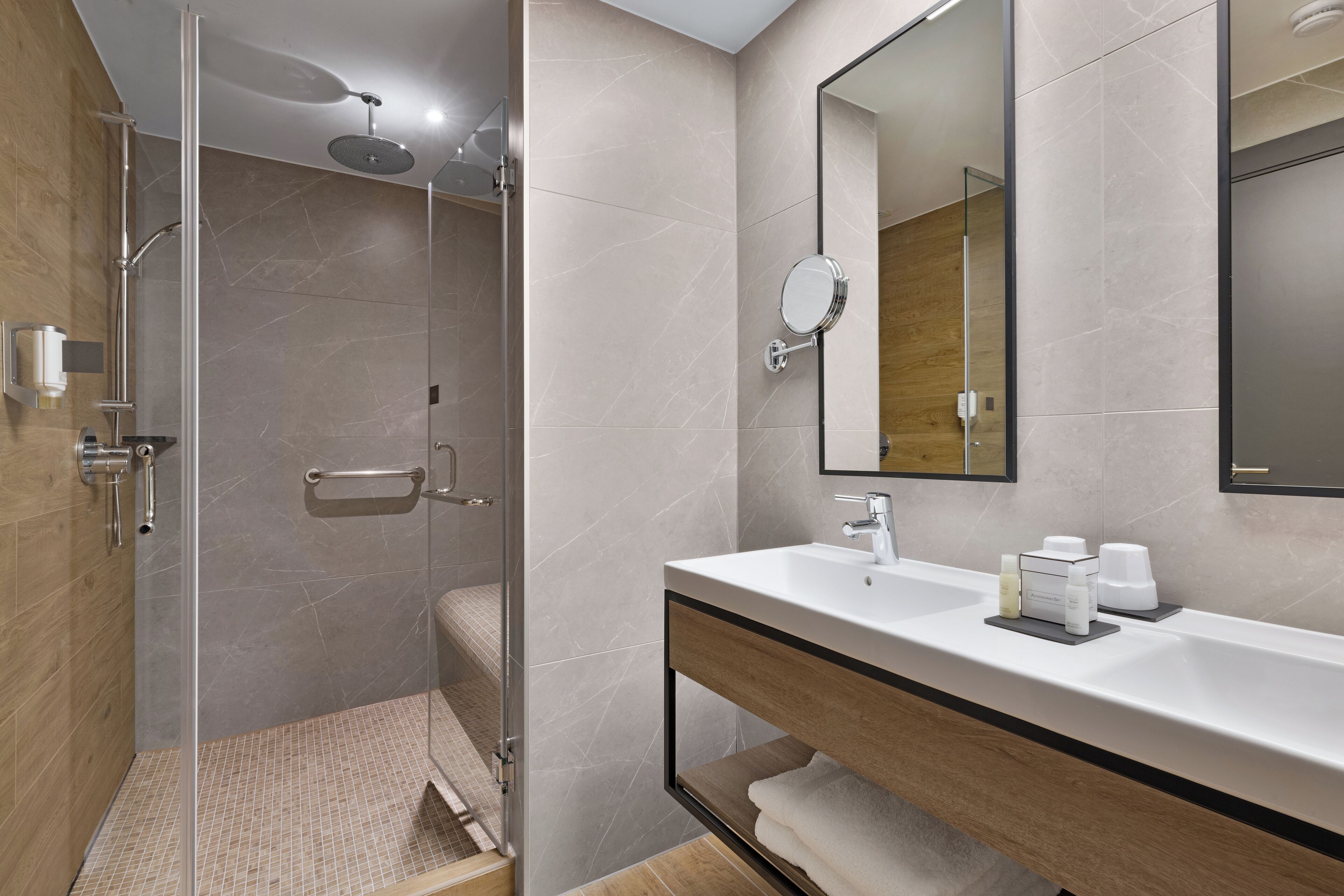 Une salle de bain moderne avec une douche à parois de verre, un lavabo blanc doté d’un meuble-vasque en bois et un grand miroir.