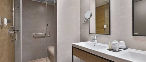 A modern bathroom with a glass-enclosed shower, a white sink with a wooden vanity, and a large mirror.