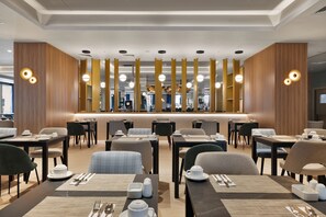 A modern hotel dining area with neatly arranged tables and chairs, a central counter, and ambient lighting.