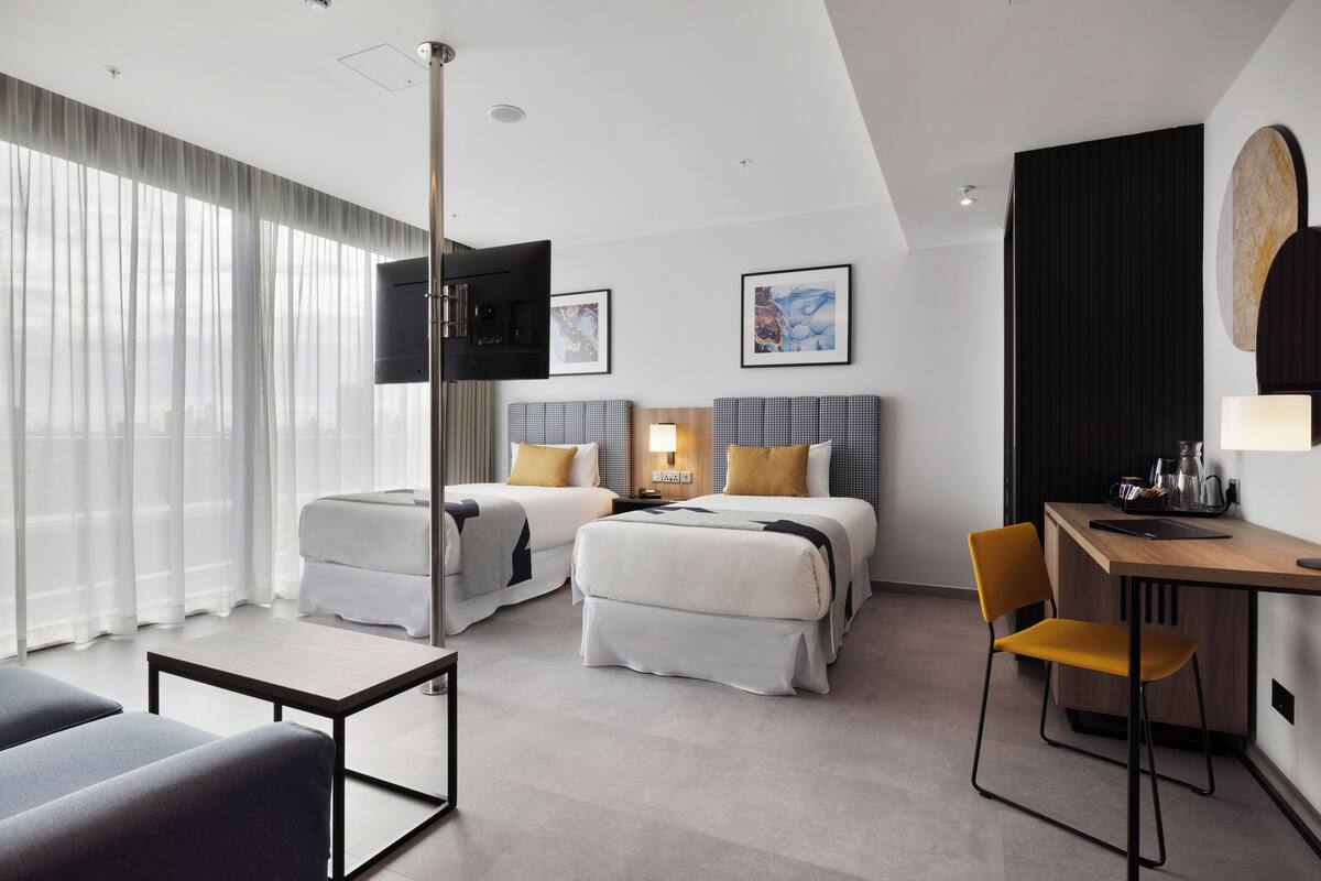 A modern hotel room with two beds, a desk, a chair, and a TV.