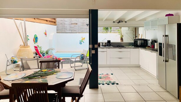 A modern kitchen with white cabinets, stainless steel appliances, and a dining area with a table and chairs. - KS VILLA (Saint-François)