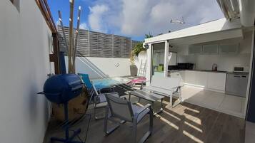 Un patio moderno con una parrilla, asientos exteriores y una cocina con armarios blancos y un microondas.