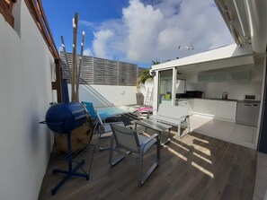 A modern patio with a barbecue grill, outdoor seating, and a kitchen area with white cabinets and a microwave. - KS VILLA (Saint-François)