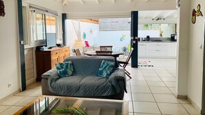 A living room with a sofa, a coffee table, and a view into a kitchen and dining area. - KS VILLA (Saint-François)