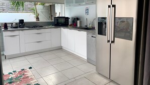 A modern kitchen with white cabinets, a stainless steel refrigerator, a microwave, and a gas stove. - KS VILLA (Saint-François)