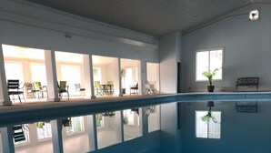 An indoor swimming pool with clear reflections, a ceiling with recessed lighting, and a view of the adjacent room with chairs and a table. - Rustic, private A-frame chalet tucked in the woods - 4 miles to town! (Berkeley Springs)
