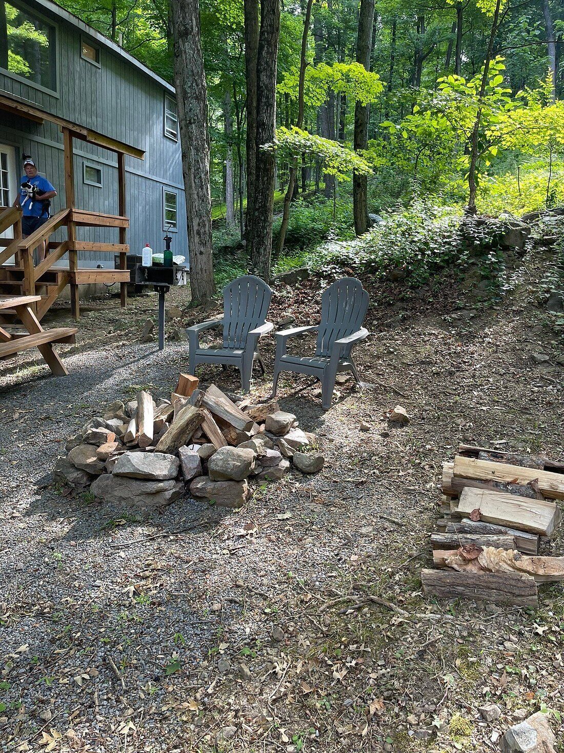 A cabin with Adirondack chairs and a fire pit in a forested area.