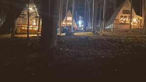 A row of cabins in a forest at night, with lights on. - Rustic, private A-frame chalet tucked in the woods - 4 miles to town! (Berkeley Springs)