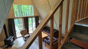 A loft-style room with a wooden staircase, a fireplace, and a view of the outdoors. - Rustic, private A-frame chalet tucked in the woods - 4 miles to town! (Berkeley Springs)