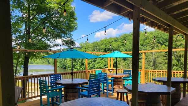 An outdoor deck with wooden tables and chairs, surrounded by a wooden railing. - Rustic, private A-frame chalet tucked in the woods - 4 miles to town! (Berkeley Springs)