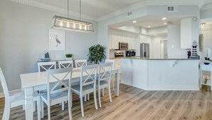 A modern kitchen with white cabinetry, a central island, and a dining area with white chairs and a table.
