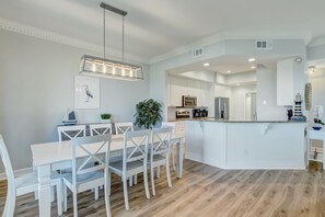 Een moderne keuken met witte kasten, een centraal eiland en een eethoek met witte stoelen en een tafel.