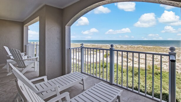 A balcony with white chairs and a view of the beach.