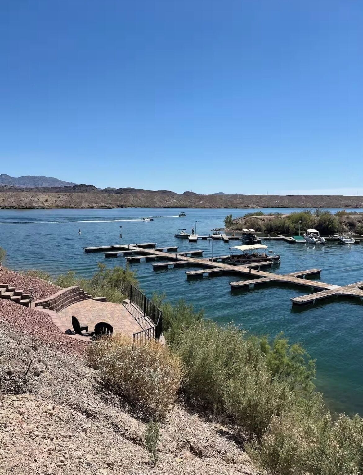 A marina with docked boats, a clear blue sky, and a mountainous backdrop.