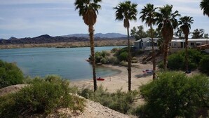A beach with palm trees, a clear blue lake, and mountains in the background.