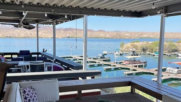 A covered outdoor seating area with a view of a marina and mountains.