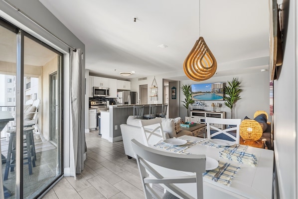 A modern kitchen with a central island, a dining area with a white table and chairs, and a living area with a sofa and a TV. - Myrtle Beach Resort by Elliott Realty (Myrtle Beach)