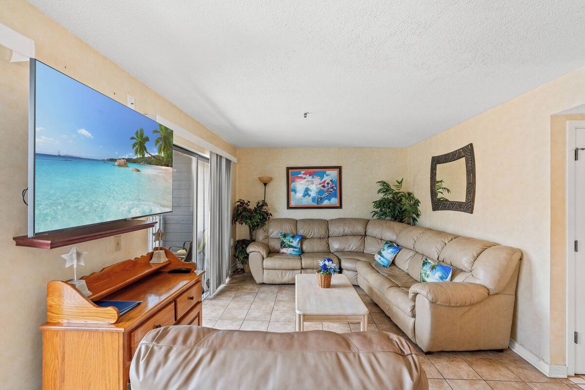 A living room with a large flat-screen TV, a beige leather sofa, a wooden coffee table, and a TV stand with a star-shaped ornament.