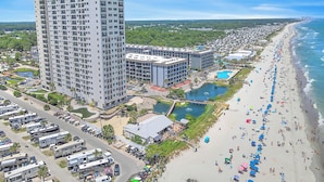 A high-rise hotel with multiple floors, a beach with umbrellas, and a parking lot with RVs. - Myrtle Beach Resort by Elliott Realty (Myrtle Beach)
