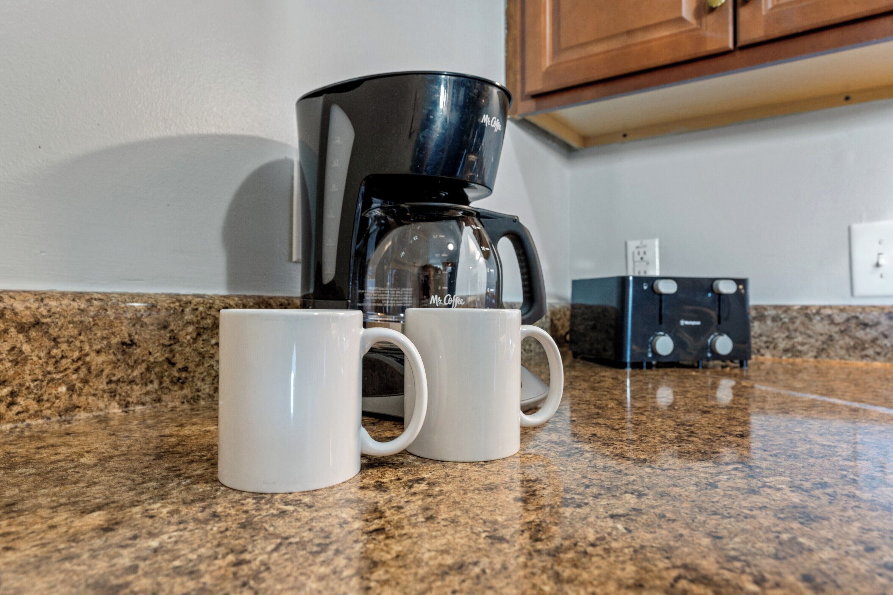 Une cuisine équipée d’une machine à café, de deux tasses blanches et d’un four à micro-ondes, le tout posé sur un plan de travail en granit.