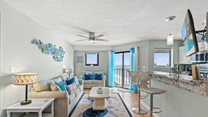 A living room with a sofa, coffee table, and a dining area with bar stools. - Myrtle Beach Resort by Elliott Realty (Myrtle Beach)