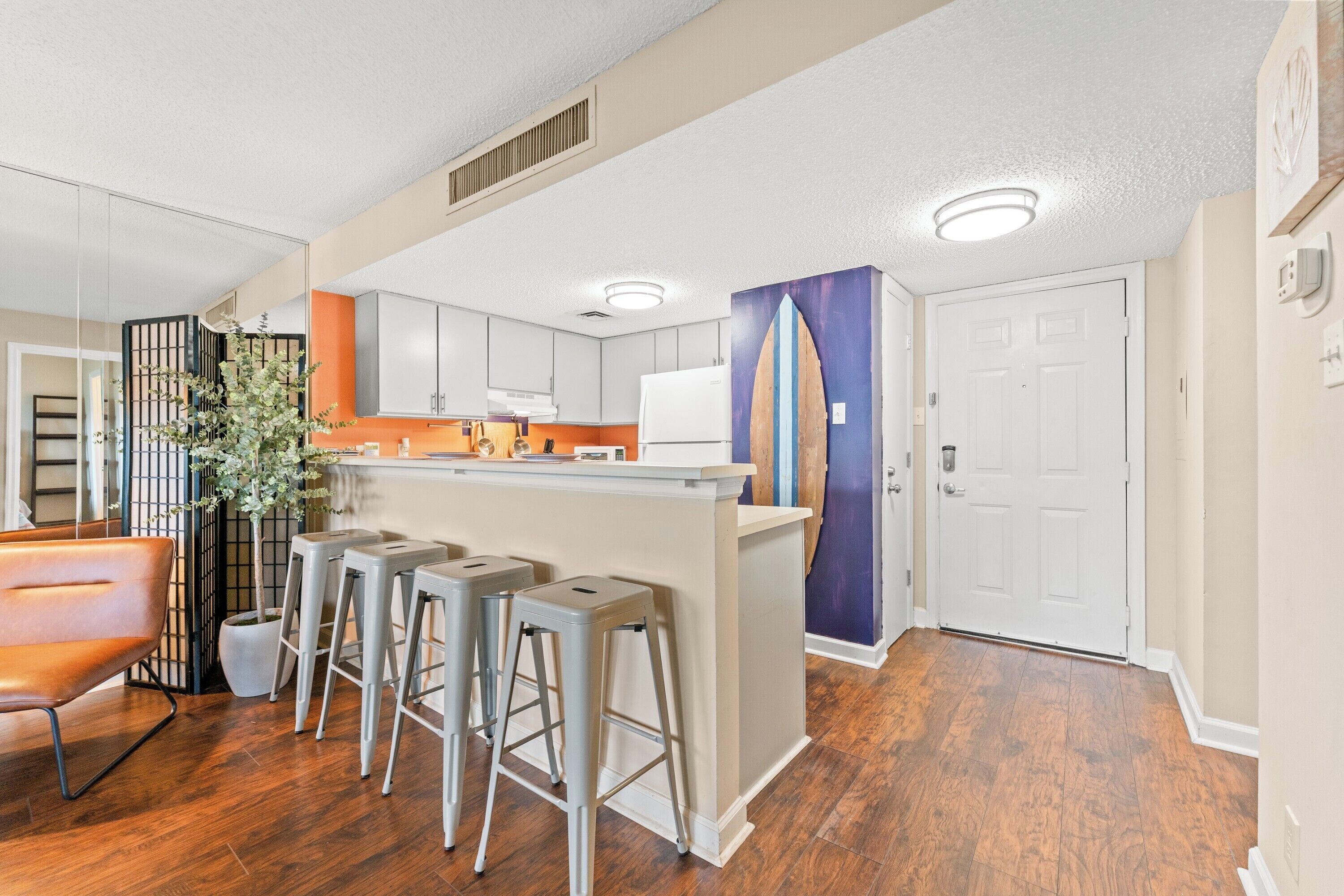 A modern kitchen with bar stools, a refrigerator, and a decorative surfboard.